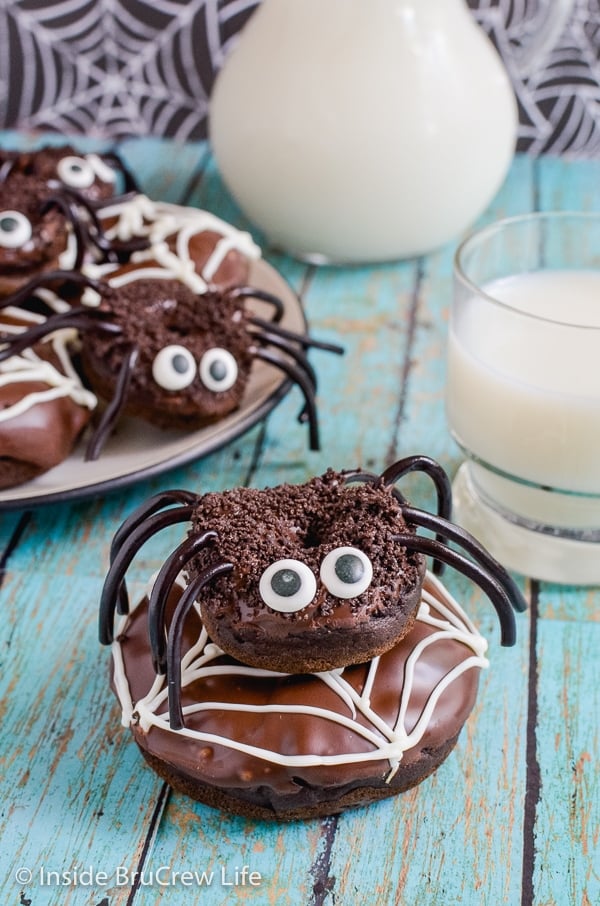 A chocolate spider donut stacked on top of a chocolate donut with a white spider web decoration