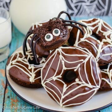 A white plate with chocolate pumpkin spider donuts stacked on it
