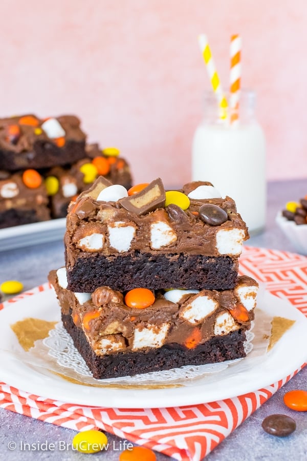 A white plate on an orange and white towel with two fluffernutter fudge brownies on it and bottle of milk behind it