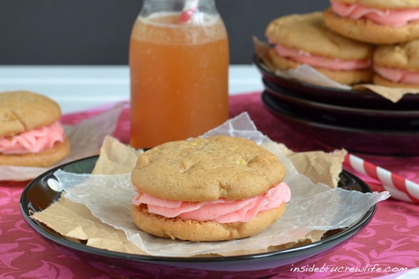 A black plate with an apple cider whoopie pie filled with red hot buttercream in it and a glass of apple cider behind it