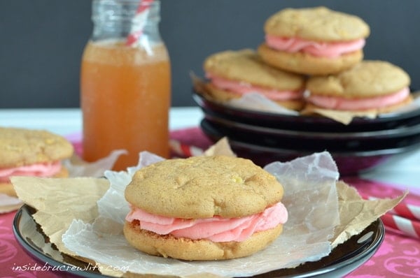 A black plate with an apple cider whoopie pie filled with red hot buttercream on it and a plate of whoopie pies behind it