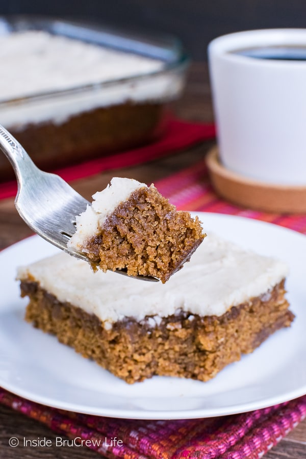 A white plate with a square of glazed apple butter cake on it and a fork lifting a bite up.