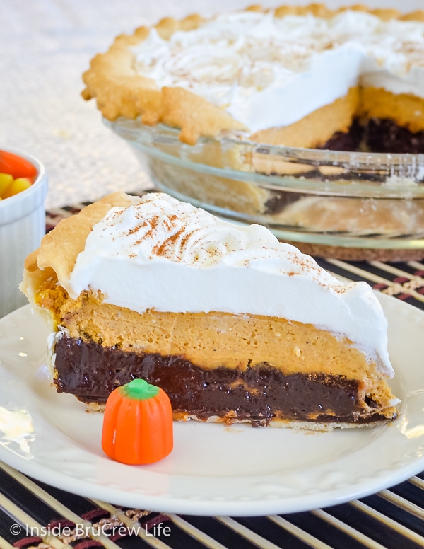 A white plate with a slice of Pumpkin Cheesecake Brownie Pie on it and the pie plate behind it