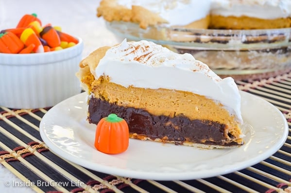 A white plate with a slice of pumpkin cheesecake brownie pie and a candy corn pumpkin on it