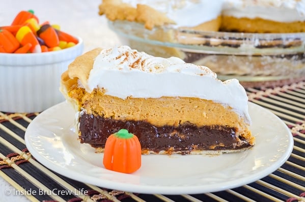 A white plate with a piece of pumpkin cheesecake brownie pie on it and the rest of the pie behind it