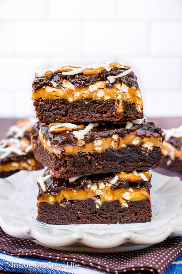 Three salted caramel brownies stacked on top of each other on a white plate.