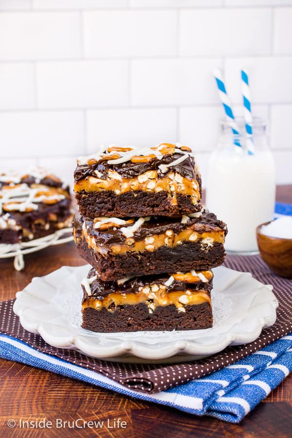 A white plate with a stack of three caramel brownies with pretzels on it.