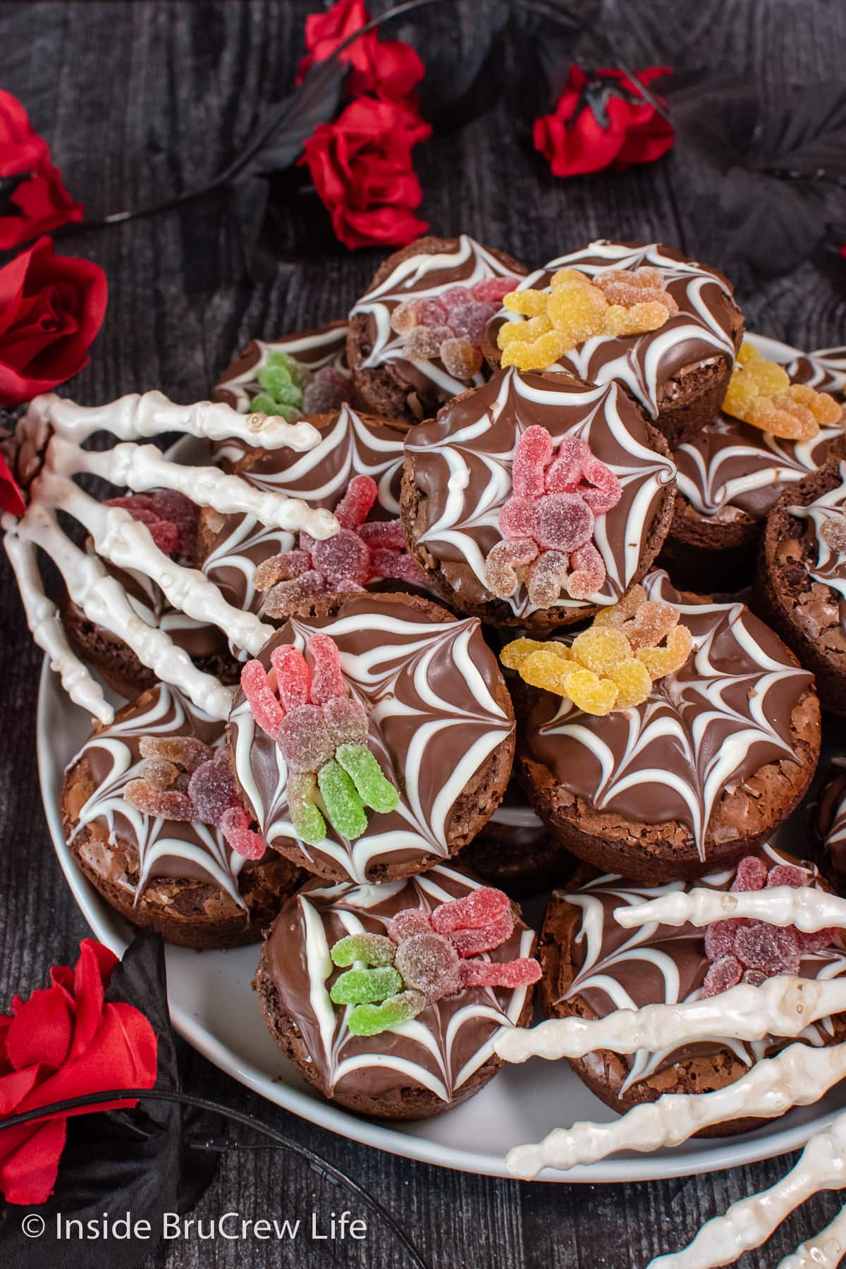 A white plate with brownie cupcakes decorated with chocolate and gummy candiesstacked on it.