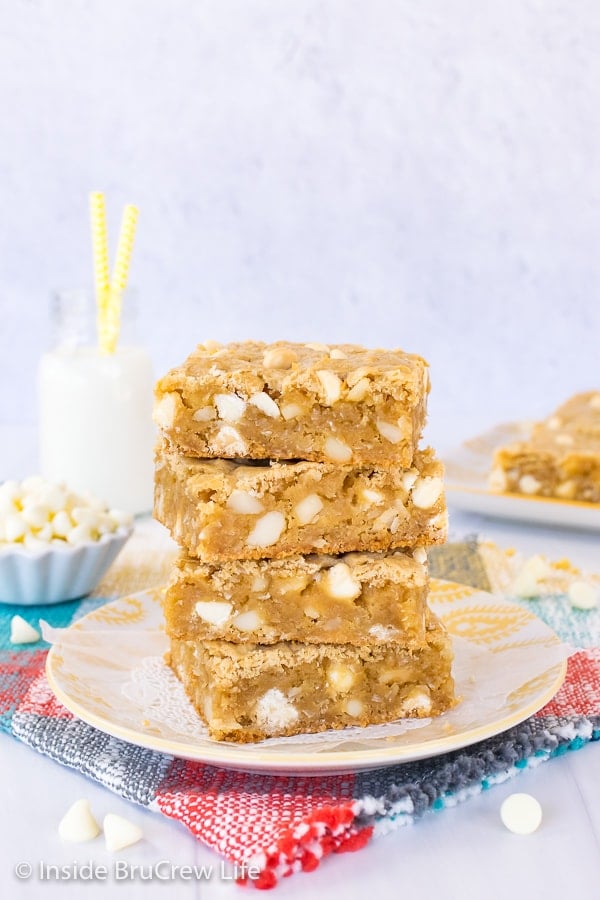 A stack of four tropical blonde brownies on a white and yellow plate with more blondies behind it