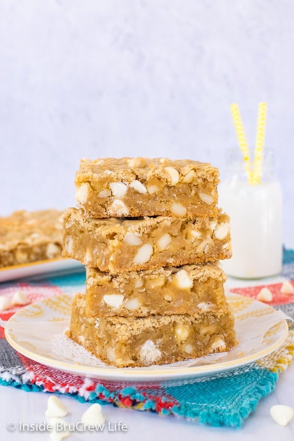 Four tropical blonde brownies stacked up on a white and yellow plate with more blondies behind it