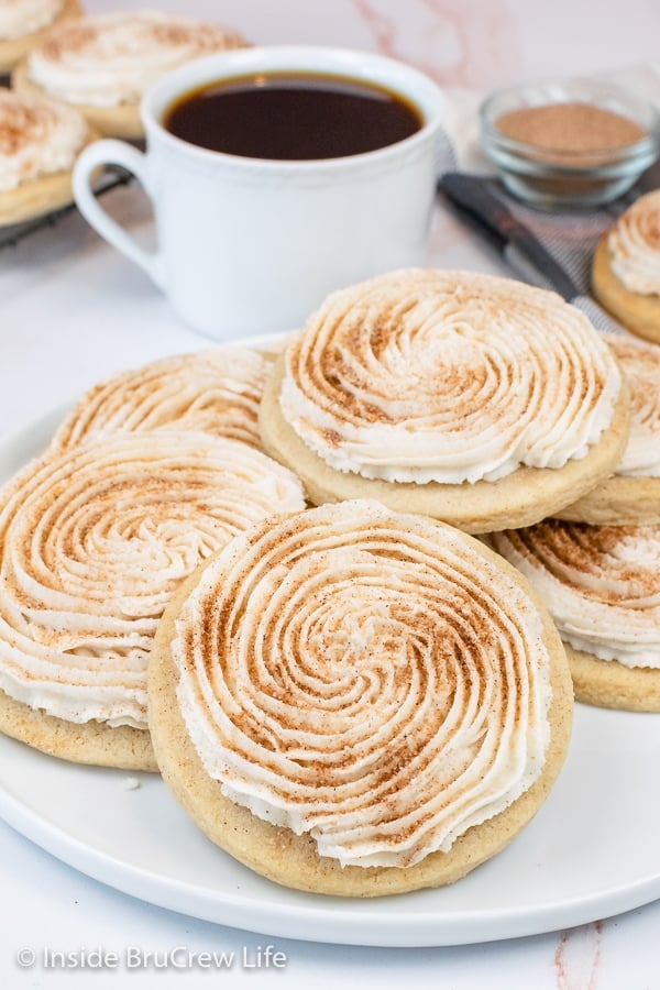 A large white plate with a bunch of frosted churro cookies stacked on it.