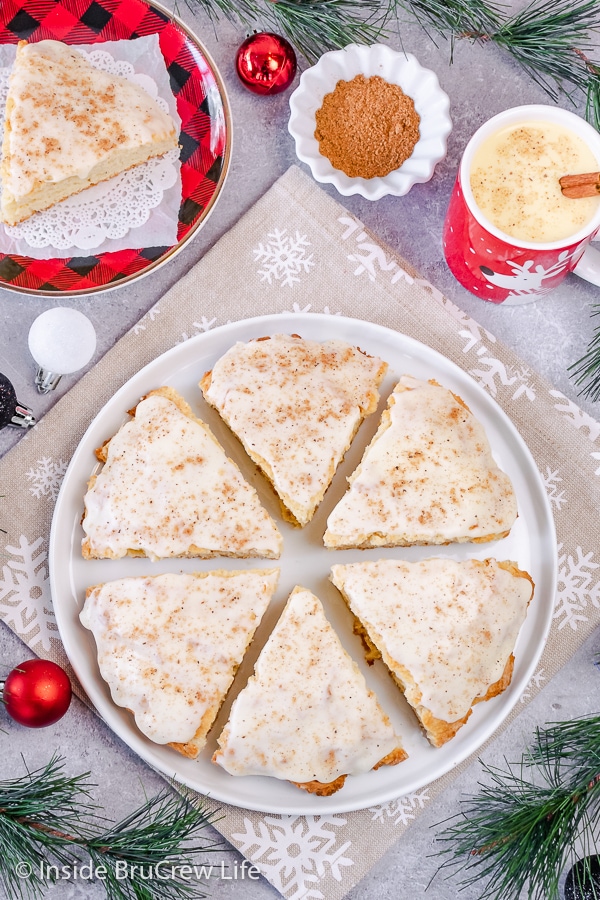 Overhead picture of a round white plate with six glazed eggnog scones topped with nutmeg on it.