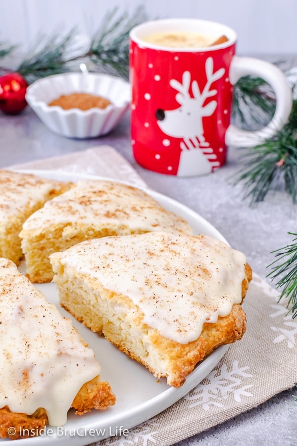 A white plate with glazed eggnog scones topped with glaze and nutmeg on it.