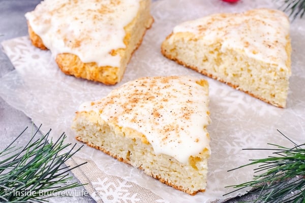 Three scones topped with eggnog glaze on a sheet of parchment paper.