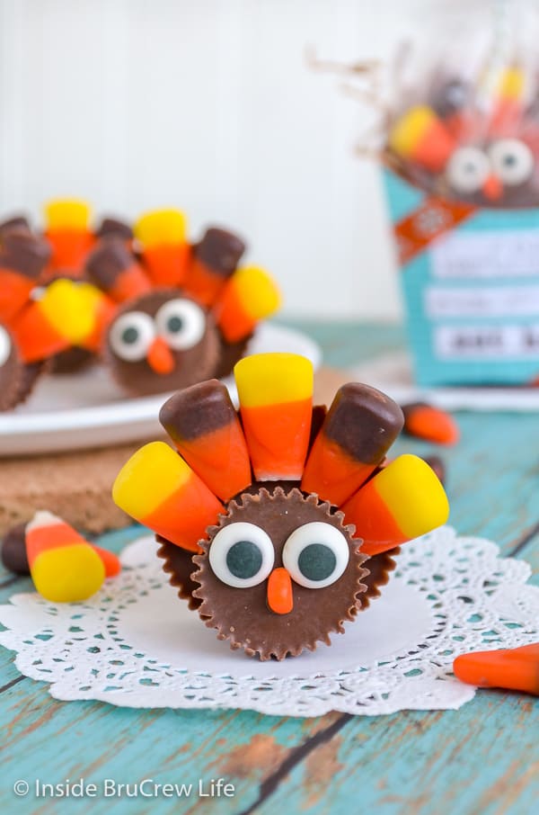 A Reese's candy turkey with candy corn tail sitting on a white paper with more turkeys behind it.