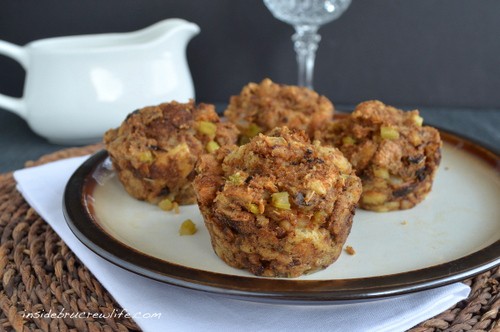 Four stuffing muffins on a plate with a container of gravy behind it