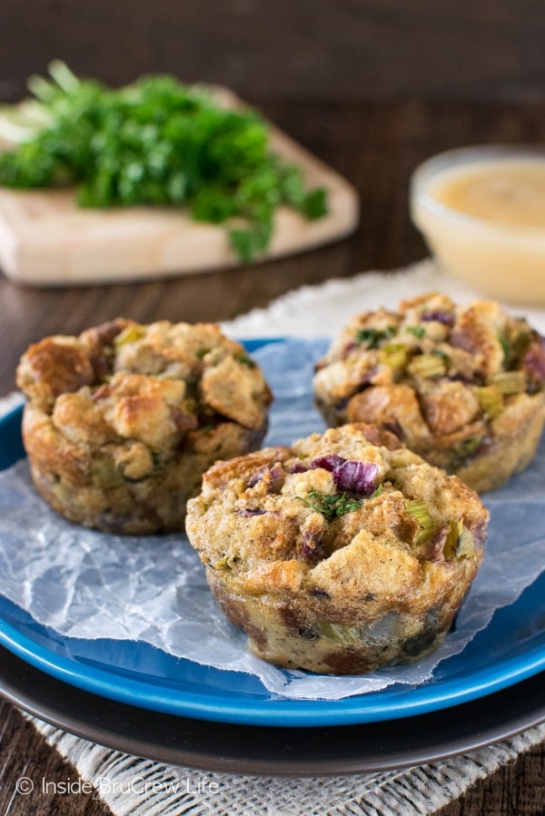 A blue plate with three stuffing muffins on it and gravy behind it