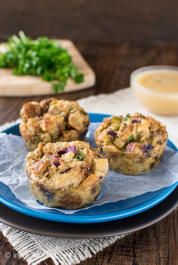 Three stuffing muffins on a blue plate with a bowl of gravy behind it