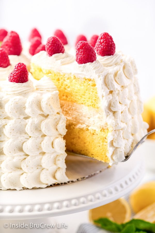 A slice of lemon cake being lifted off a cake plate.