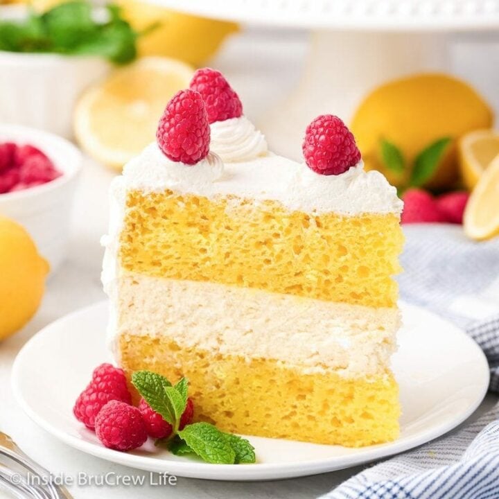 A white plate with a slice of lemon cheesecake layer cake on it.