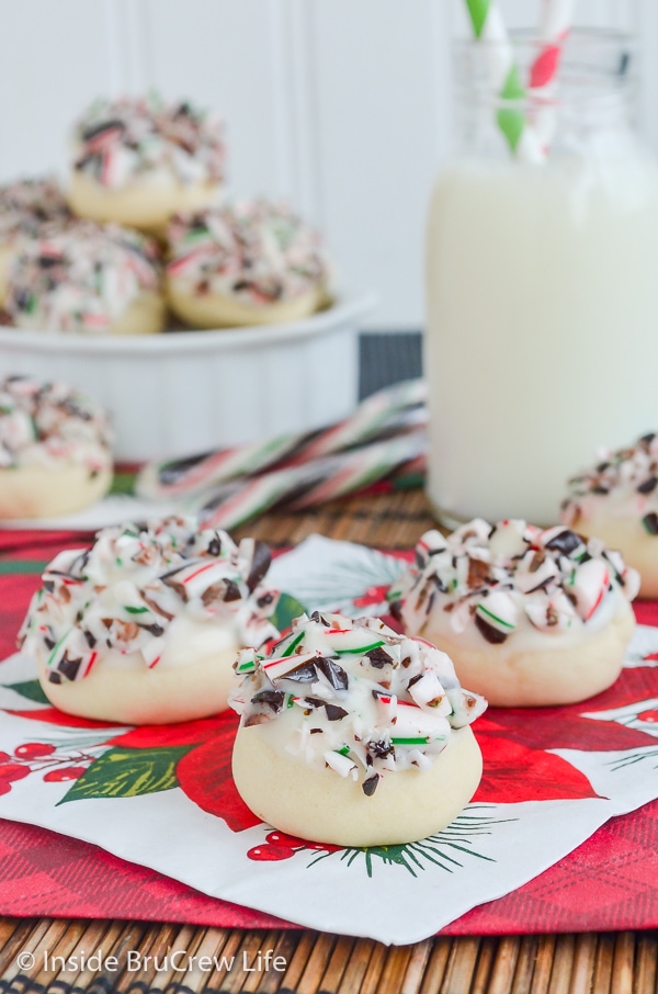 A holiday napkin with a few white chocolate peppermint snowball cookies topped with candy canes on it.