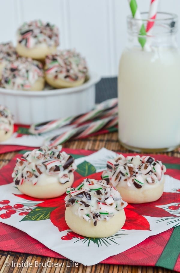 A holiday napkin with three peppermint snowball cookies topped with white chocolate and candy canes on it.