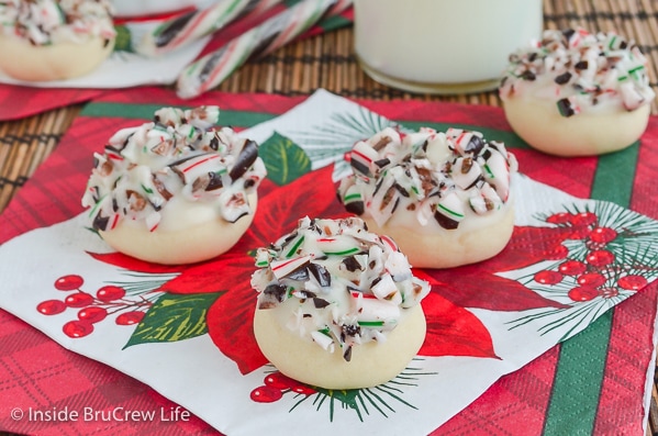 Three white chocolate dipped peppermint snowballs topped with candy canes on a holiday napkin.