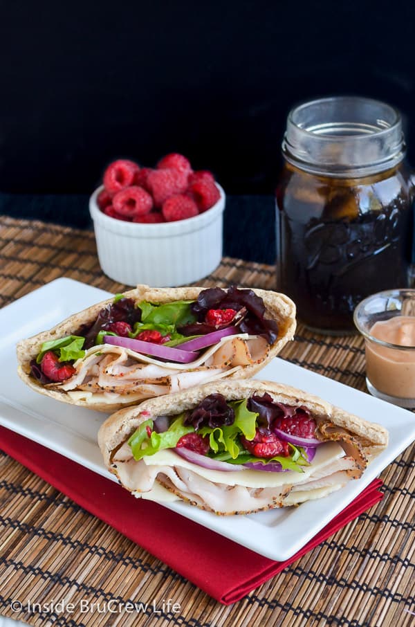 Two pita halves filled with turkey, raspberries, and salad on a white plate 