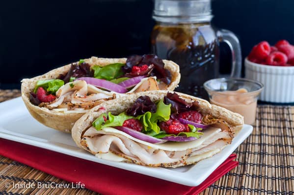 Two pita halves on a white plate filled with turkey, salad, onions, and raspberries