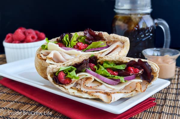 A white plate with two pita halves filled with turkey, salad, and raspberries