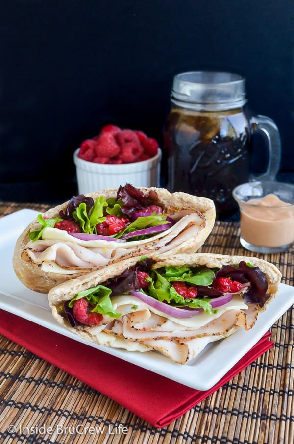 Two pita halves on a white plate filled with turkey, cheese, spring mix, and raspberries