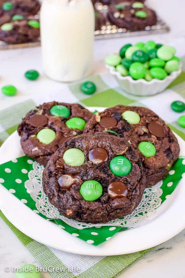 3 chocolate cookies with green candies arranged together on a white plate with a green napkin.