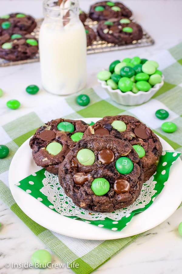 3 chocolate cookies with green candies arranged together on a white plate with a green napkin.