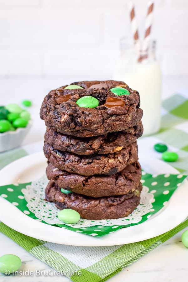 5 chocolate cookies with green candies stacked on top of each other on a white plate with a green napkin.