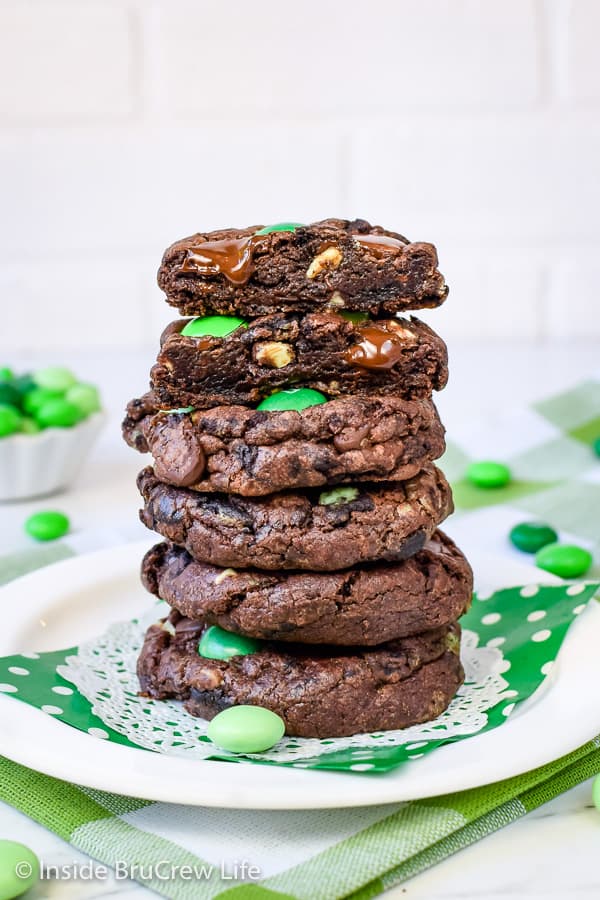 5 chocolate cookies with green candies stacked on top of each other on a white plate with a green napkin.