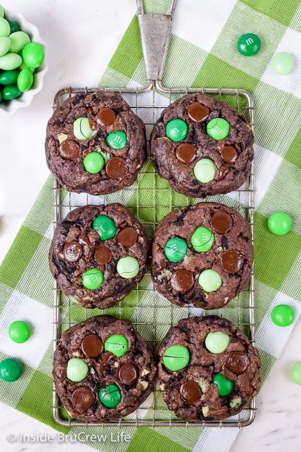 6 chocolate cookies with green candies on a wire cooling rack.