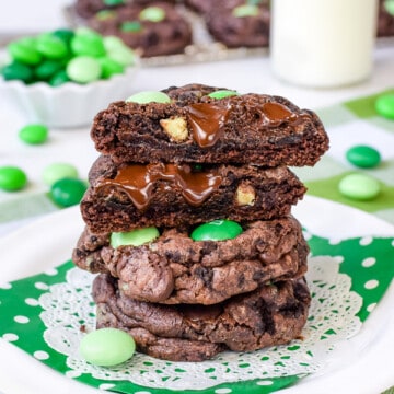 3 chocolate cookies with green candies stacked on top of each other on a white plate with a green napkin.