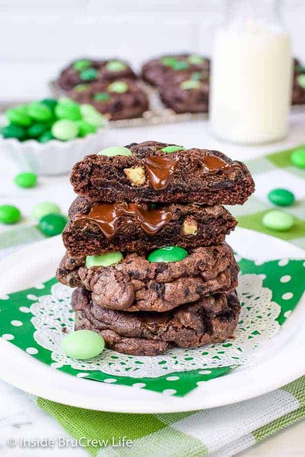 3 chocolate cookies with green candies stacked on top of each other on a white plate with a green napkin.