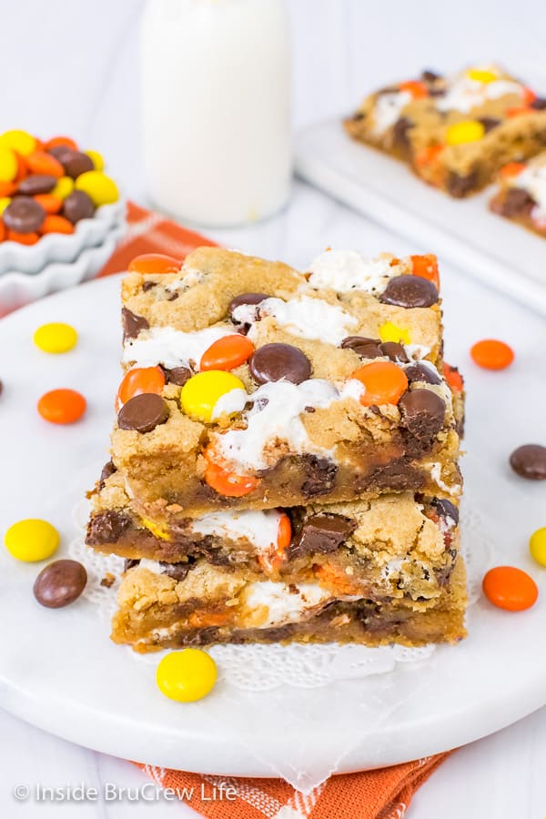 An overhead picture of three squares of Marshmallow Reese's Blonde Brownies on a white board with Reese's scattered around it