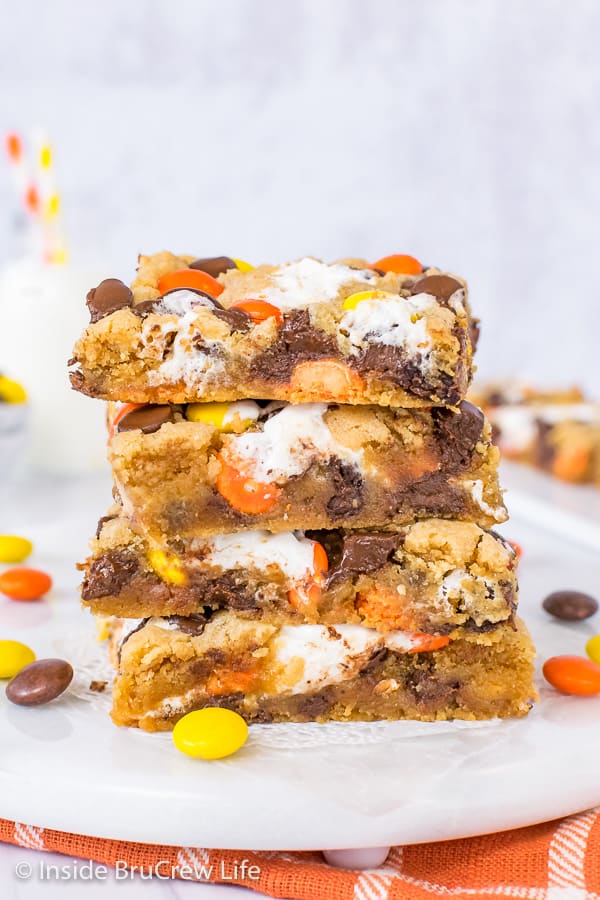 A stack of four peanut butter blonde brownies loaded with chocolate chips, marshmallow, and Reese's Pieces on a white board