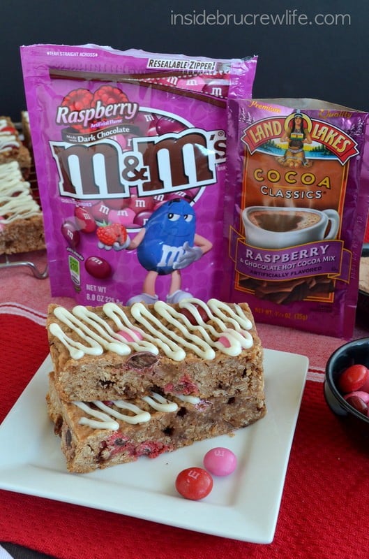 Two raspberry hot chocolate granola bars on a white plate with ingredients behind it.