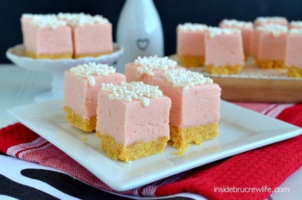 Squares of strawberry fudge with a shortbread cookie crust and white chocolate drizzle on a white plate