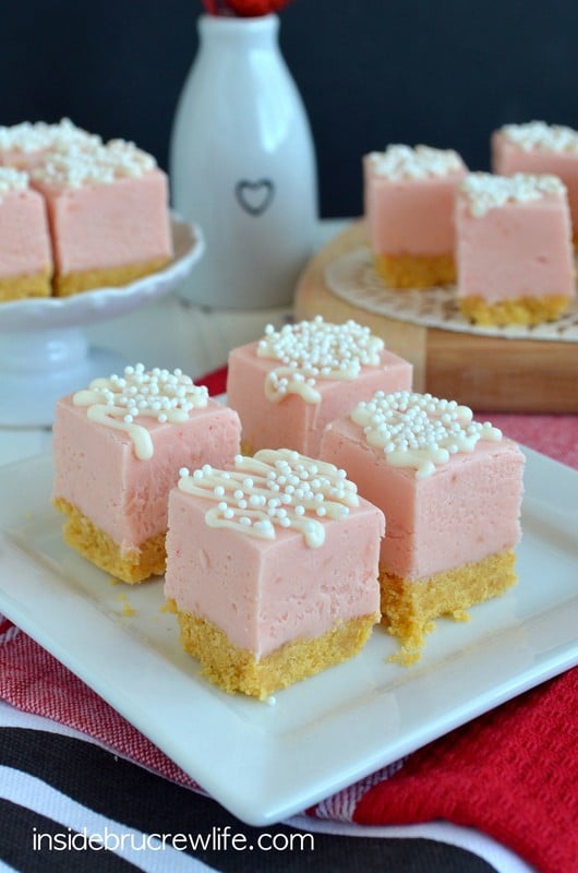 Squares of strawberry fudge with a cookie crust and white chocolate drizzles on a white plate