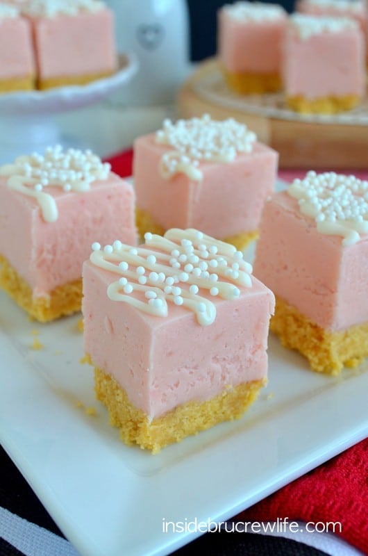 Close up picture of squares of strawberry fudge with a cookie crust and white chocolate drizzles on a white plate