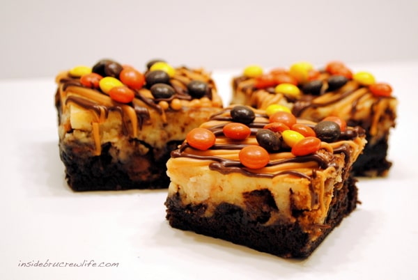 Three cheesecake brownies topped with Reese's on a white board.