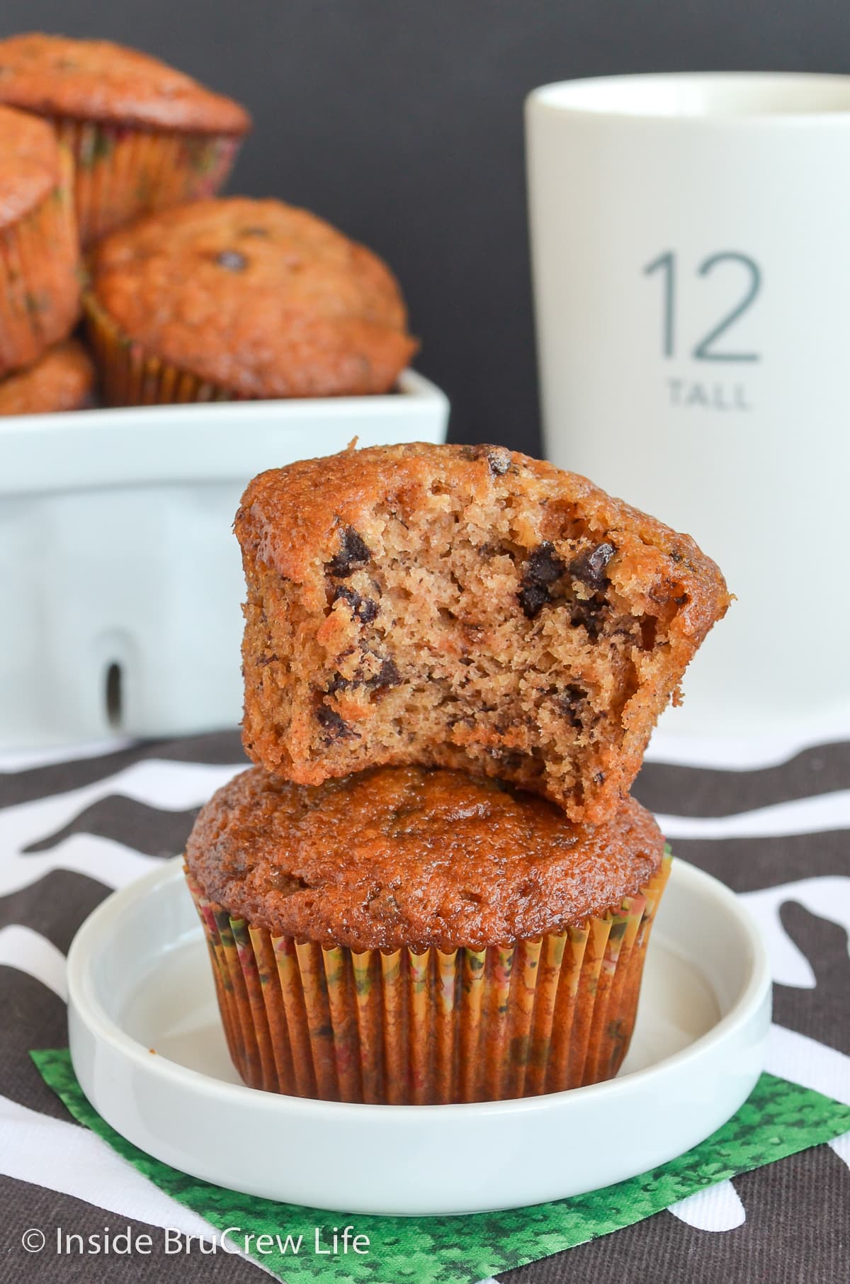 Two banana muffins stacked on a plate with a bite out of the top one.