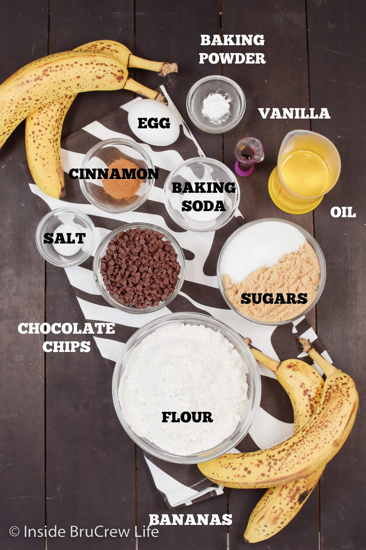 A dark board with bowls of ingredients needed to make banana muffins.