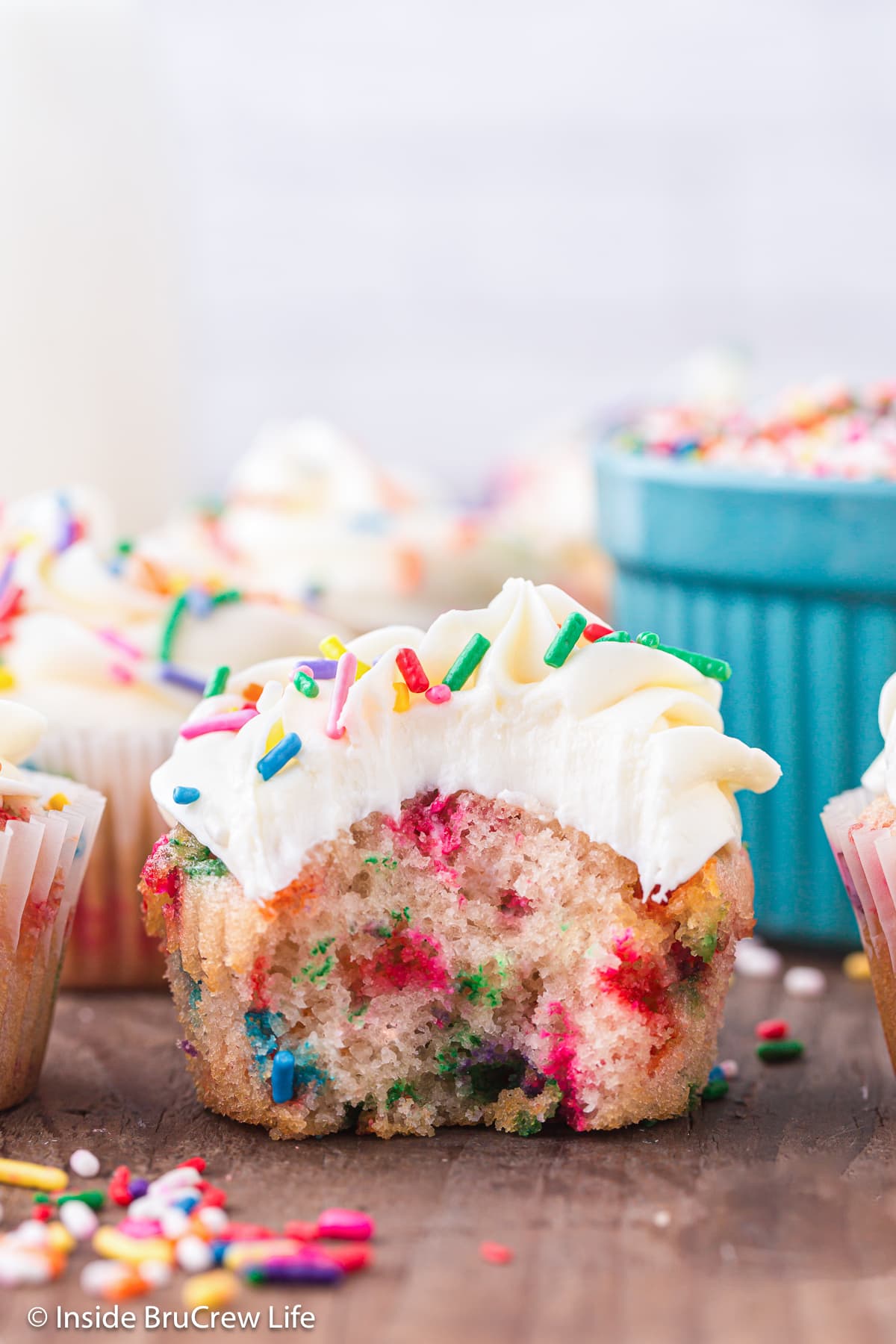 A funfetti cupcake with vanilla frosting with a bite taken out of it.