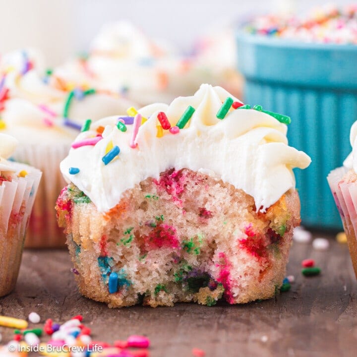 A funfetti cupcake with vanilla frosting with a bite taken out of it.