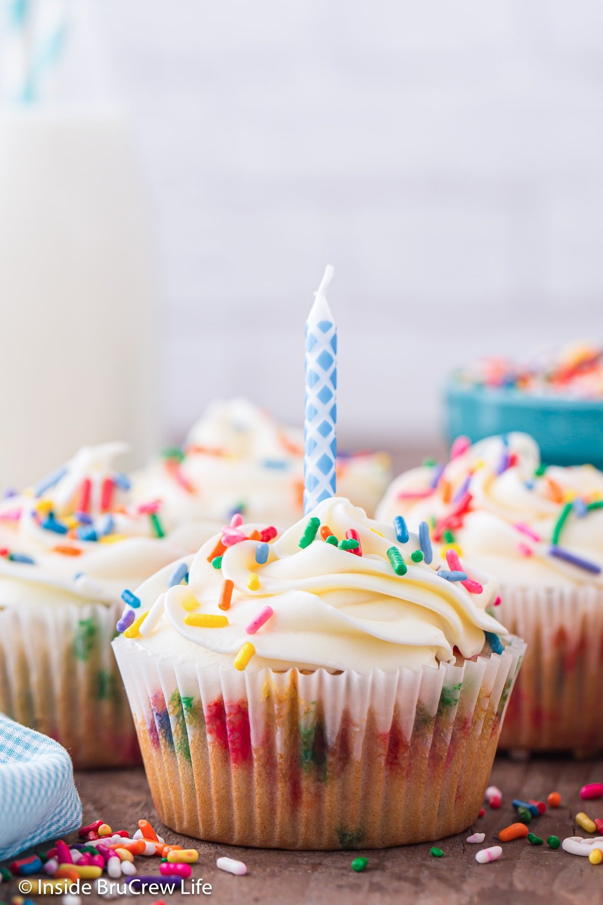 A frosted funfetti birthday cupcake topped with sprinkles and a candle.